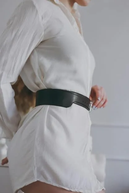 A close-up of a person's torso, featuring a bold, geometric statement belt cinching a neutral-colored oversized sweater. The focus is on the contrast and the belt's intricate design, highlighting how a single accessory can transform a simple outfit.