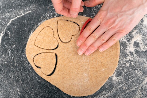 Overhead shot of hands rolling out dog treat dough on a floured surface with a rolling pin and bone-shaped cookie cutters nearby.