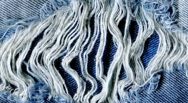 Close-up of denim jeans exhibiting intricate distressing with exposed horizontal white threads and neatly frayed edges, showcasing a professionally achieved DIY distressed look.