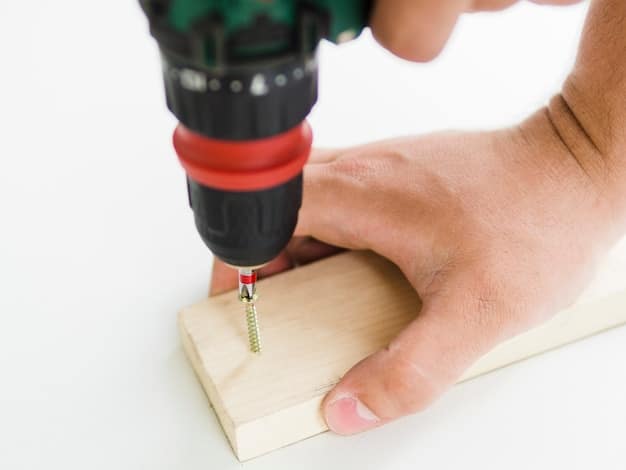 A close-up shot of hands using a power drill to carefully screw together two pieces of scrap wood, forming the side of a birdhouse. Wood shavings are visible on the workbench around the partially assembled structure.