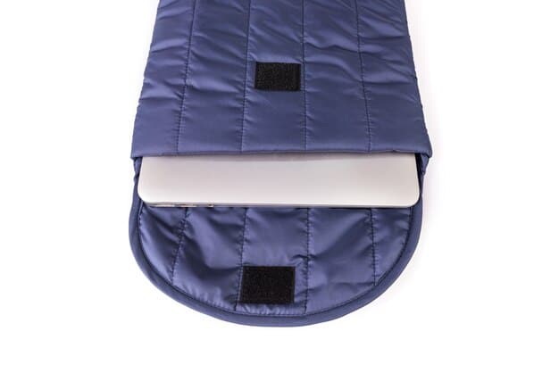 A close-up of a quilted laptop sleeve with a small, neatly stitched external pocket, showing a charging cable peeking out, illustrating added functionality.