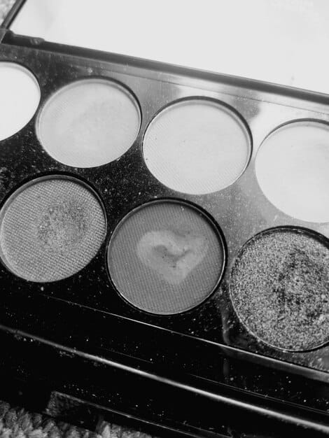 A close-up shot of an eyeshadow palette featuring various shades of gray, black, and silver, alongside an array of makeup brushes, emphasizing the tools needed for a smokey eye.