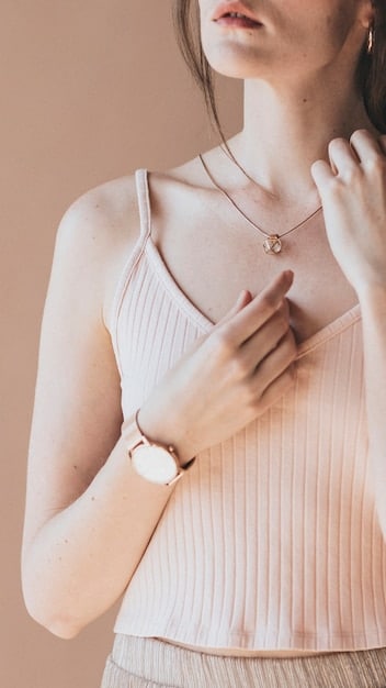 Close-up of hands accessorizing an outfit, showing a person adding a delicate necklace and a classic watch to a simple yet elegant blouse, focusing on the refined details.