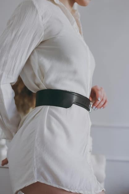 A close-up of a person's torso, featuring a bold, geometric statement belt cinching a neutral-colored oversized sweater. The focus is on the contrast and the belt's intricate design, highlighting how a single accessory can transform a simple outfit.