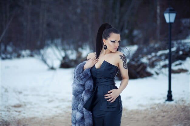 A person elegantly draped in a luxurious, dark velvet evening gown, accessorized with a subtle diamond necklace and a black faux fur stole, hinting at a winter formal event.