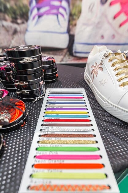 A digital render of a sneaker being customized on a screen, with various material swatches and color palettes displayed around it.