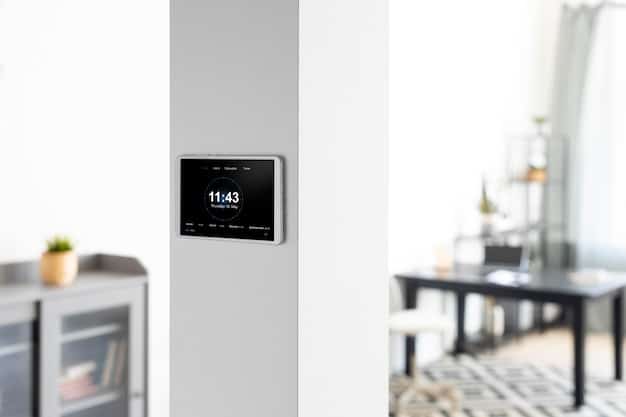 A sleek smart thermostat on a wall in a modern home, displaying the temperature, with a blurred background of an open-plan kitchen and living area, suggesting seamless climate and lighting control.